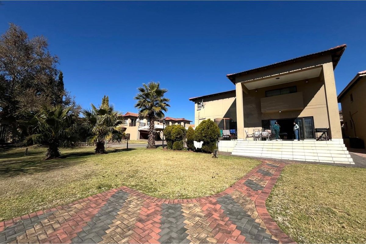 Rear view of the house featuring a covered patio, tiled steps, and a landscaped garden with a paved walkway.