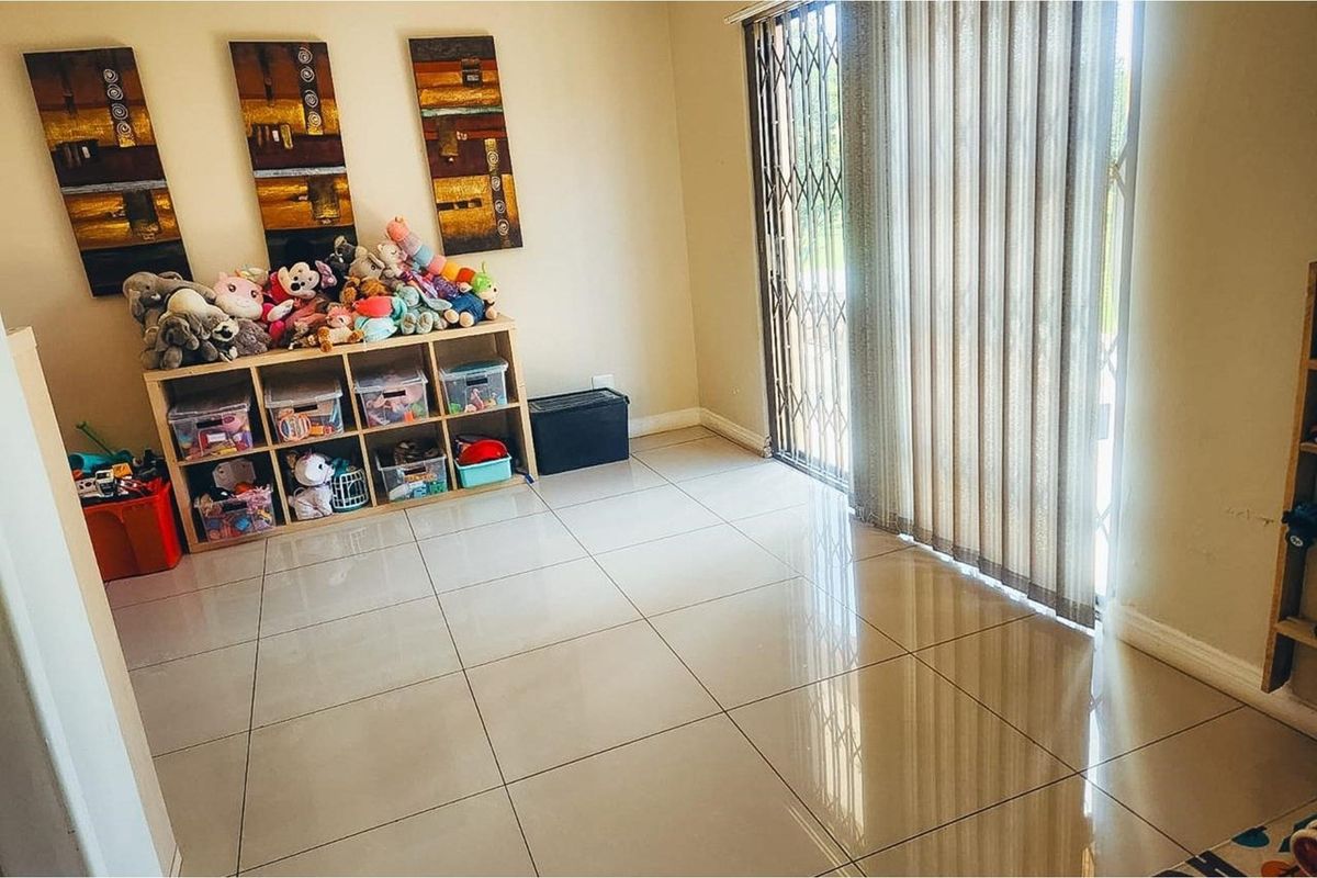 A bright living area featuring large format floor tiles and a sliding glass door with a security gate leading to the outdoors.