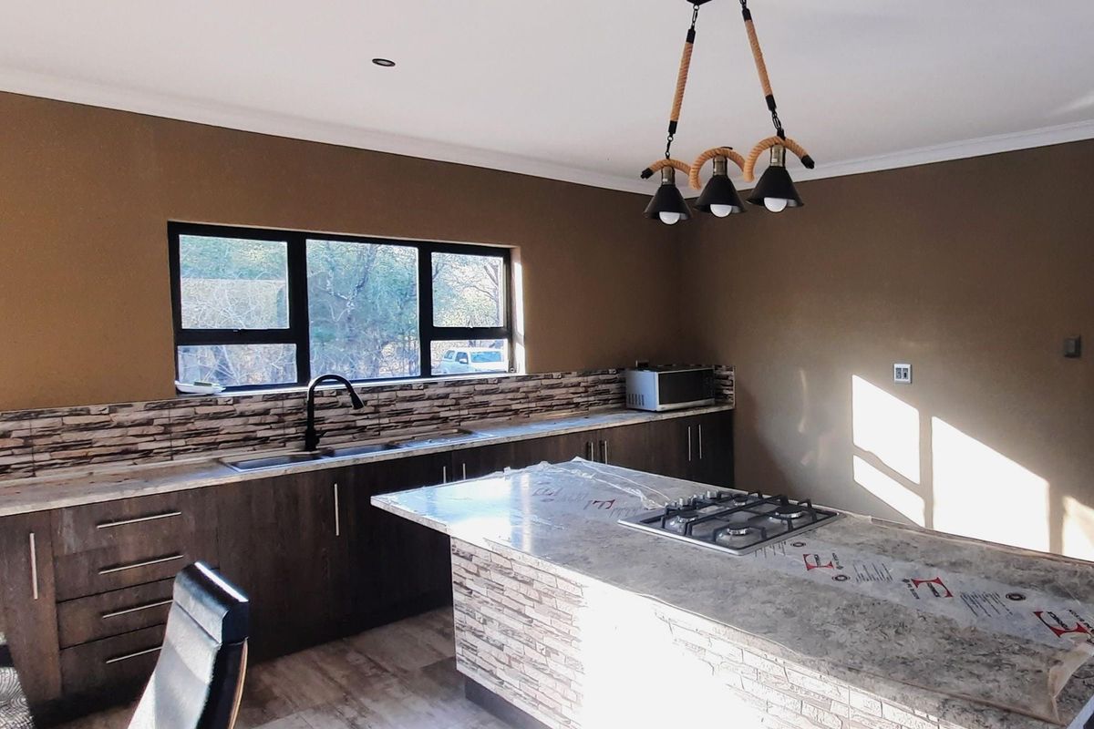 Modern kitchen featuring a central island with a built-in gas hob, stone-look countertops, dark cabinetry, and a tiled backsplash.