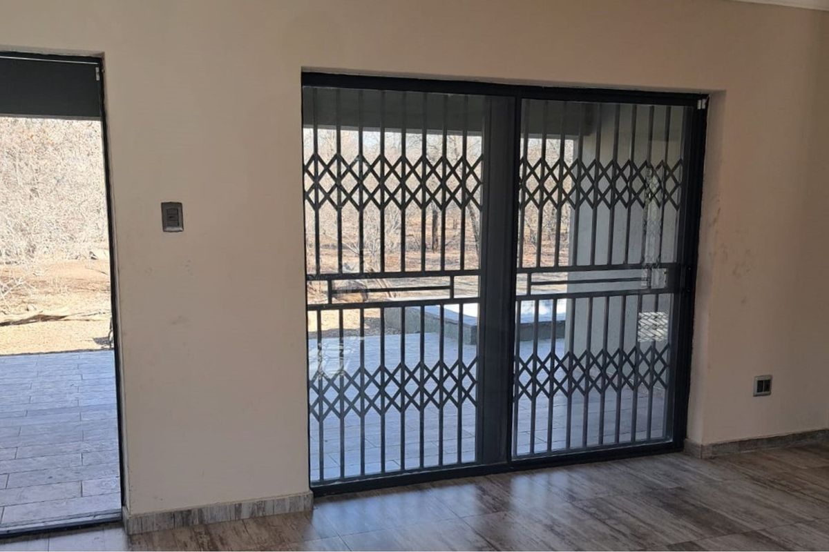 Interior view of a living area featuring tiled flooring and sliding glass doors secured with metal security gates, providing access to an outdoor patio.