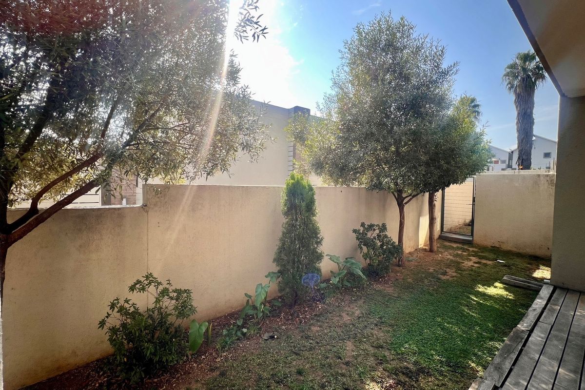 A private rear garden area featuring a boundary wall, established trees, and a small lawn space accessible from the patio.