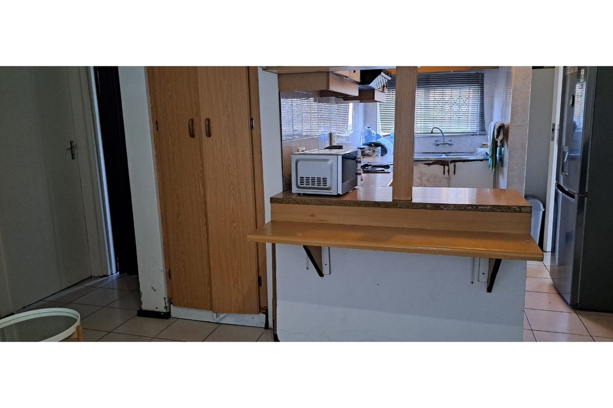 A dated kitchen featuring a breakfast bar, laminate countertops, and tiled flooring, requiring cosmetic updates to modernize the space.
