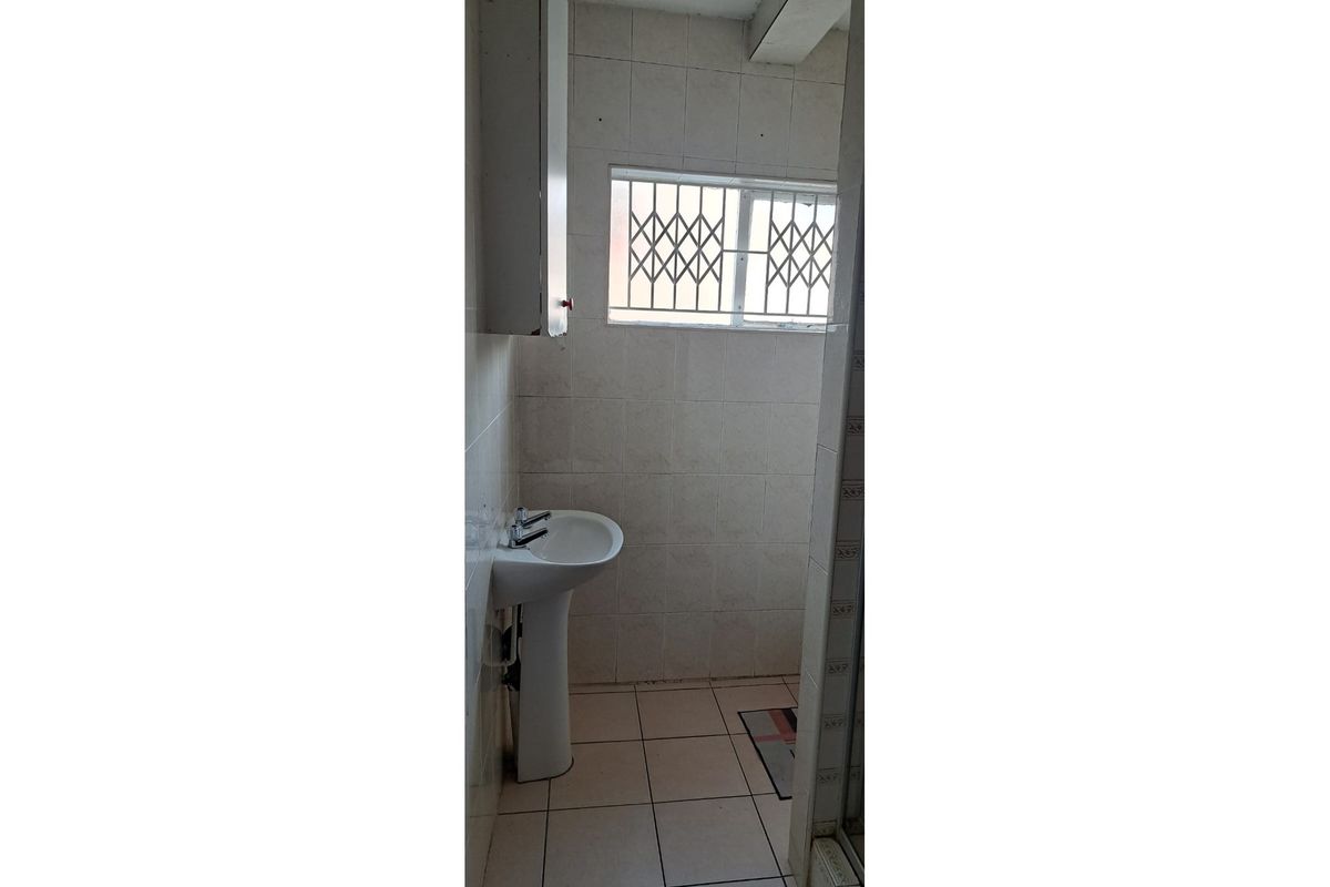 A compact bathroom featuring a pedestal basin, tiled walls and flooring, and a window fitted with a security gate.