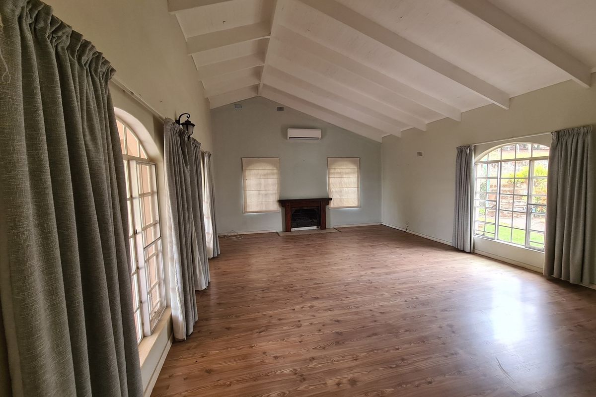 Spacious living room featuring vaulted ceilings with exposed beams, wood-look flooring, a built-in fireplace, and large arched windows providing natural light.