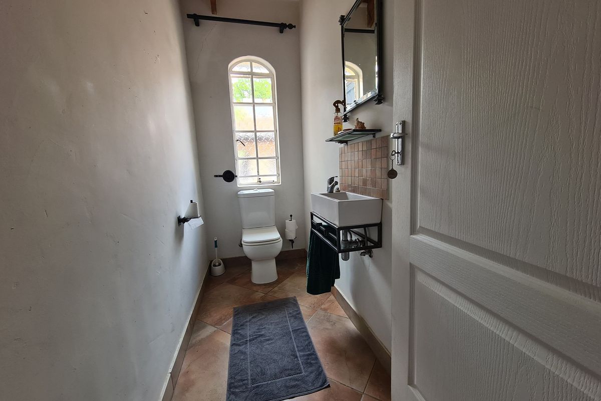 A compact guest bathroom featuring a wall-mounted basin, tiled splashback, and a toilet, finished with terracotta-style floor tiles and an arched window.