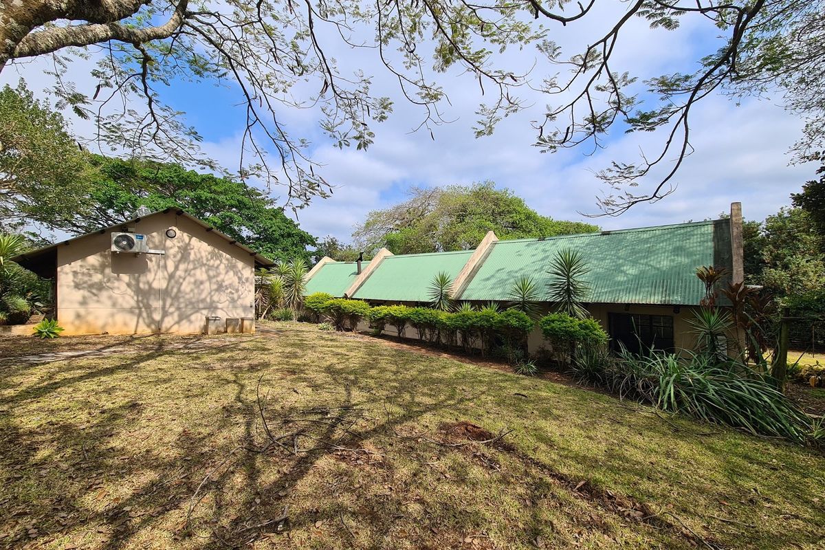 A view of the rear exterior of the farm property, featuring a pitched green metal roof, established garden, and mature trees.