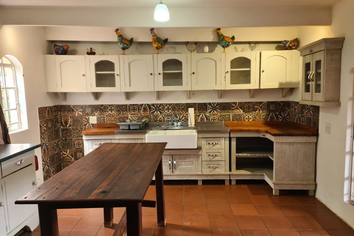 Rustic farmhouse kitchen featuring patterned tile backsplash, wooden countertops, a farmhouse sink, and white cabinetry with wire-mesh detailing.