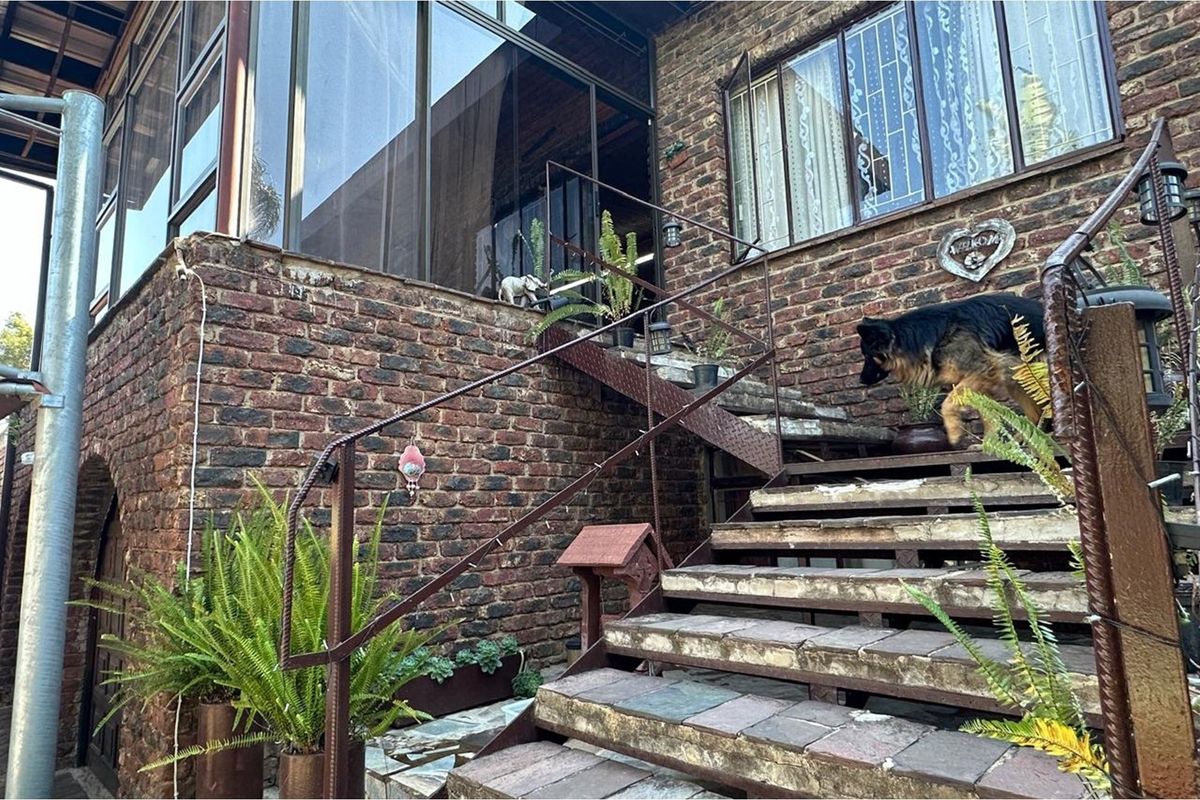 Exterior view of a brick-faced home featuring an elevated patio area accessed by a metal staircase with stone treads.