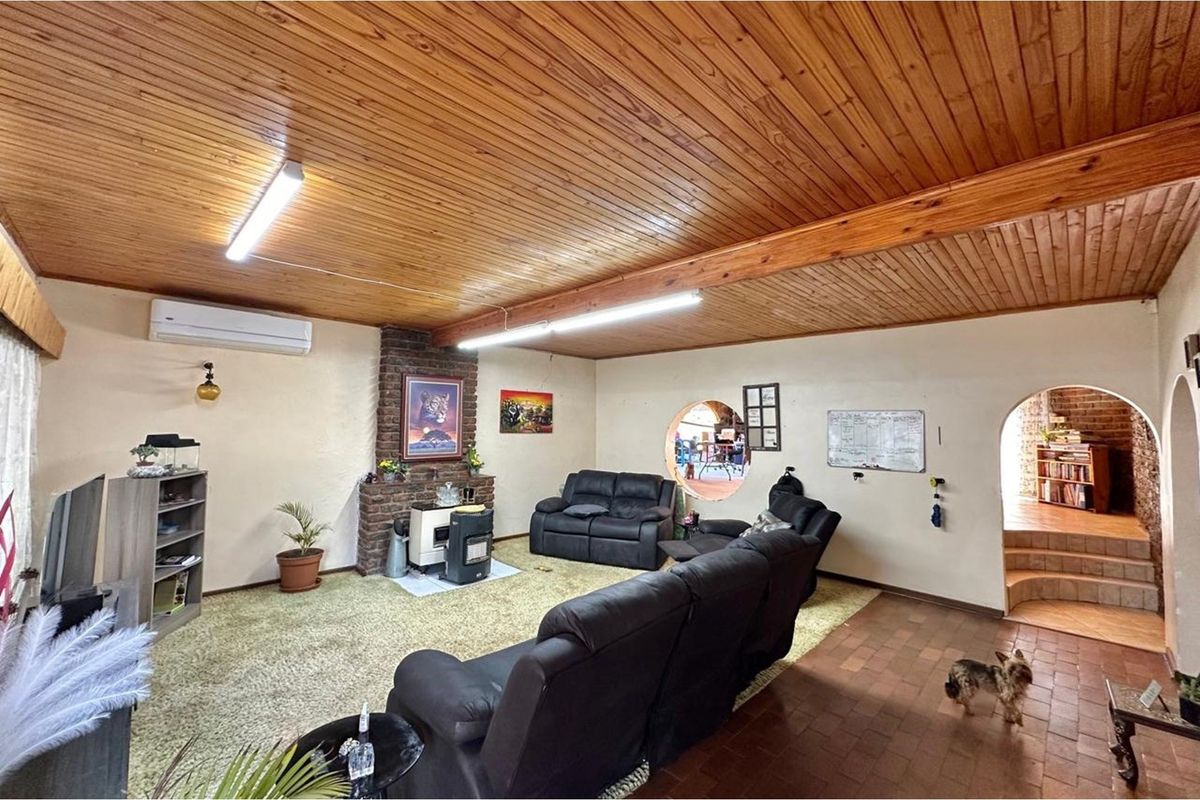 Spacious living room featuring a brick fireplace, timber-clad ceiling, split-system air conditioning, and an arched doorway leading to an adjacent area.
