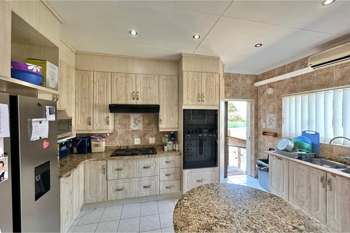 A functional kitchen featuring light wood-grain cabinetry, granite countertops, a built-in oven, hob, extractor fan, and tiled flooring with direct outdoor access.