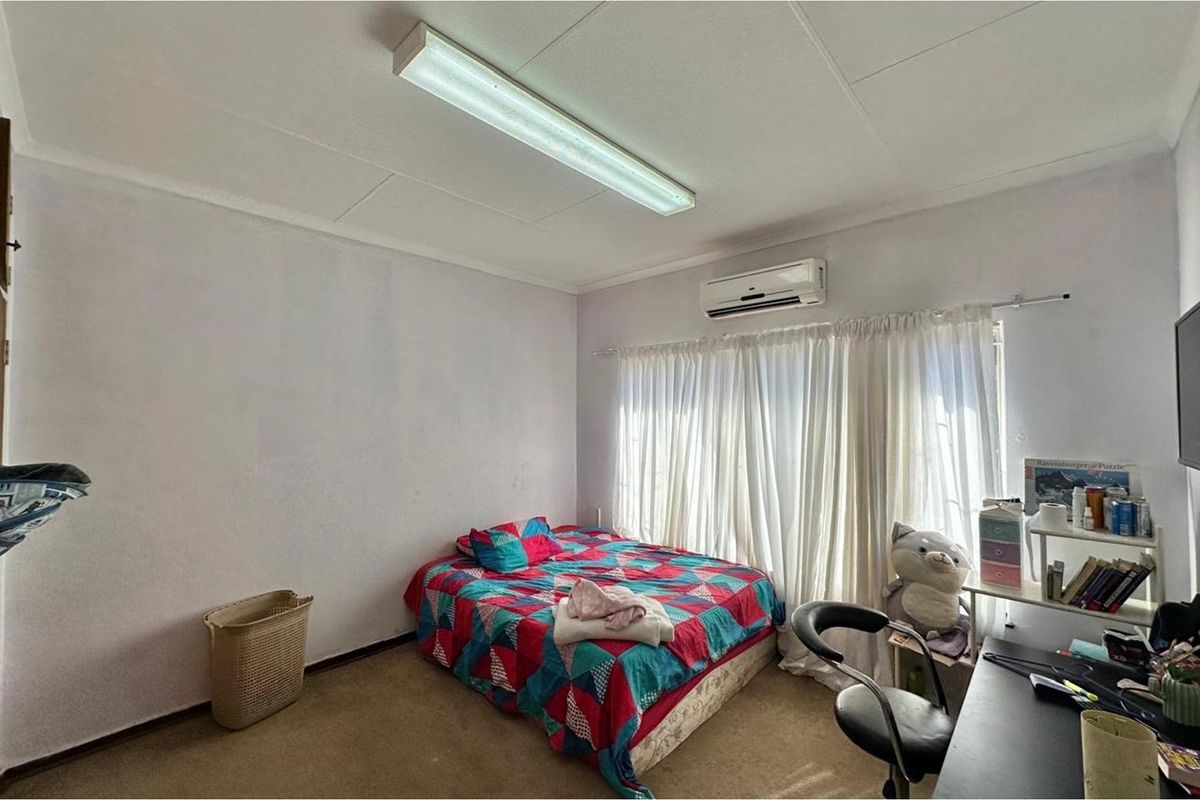 A functional bedroom featuring a wall-mounted air conditioning unit, tiled ceiling, and carpeted flooring.