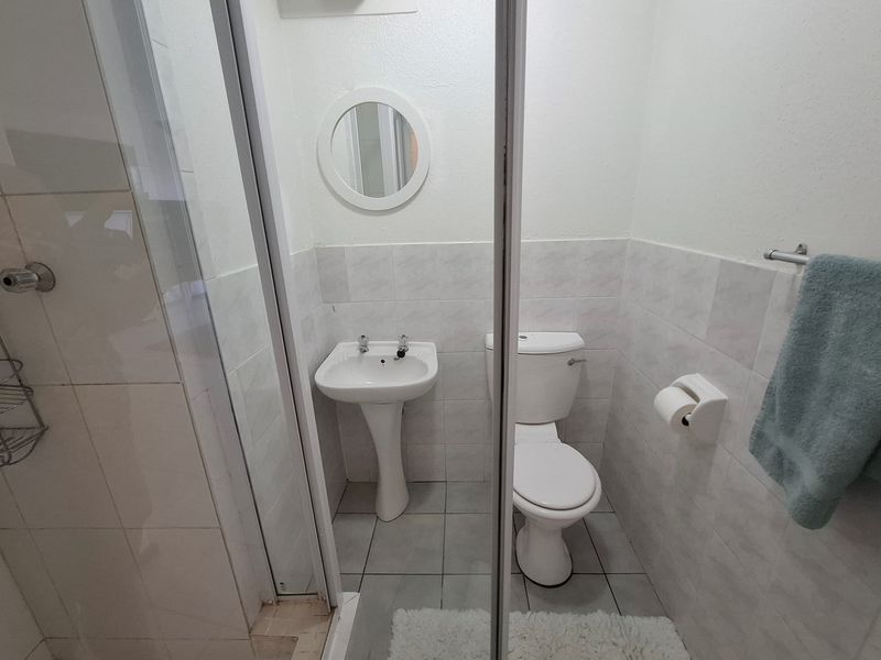Compact bathroom featuring a pedestal basin, toilet, and a glass-enclosed shower with neutral wall and floor tiling.