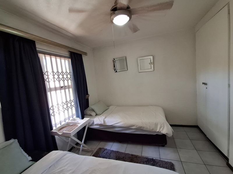 A functional bedroom featuring tiled flooring, a ceiling fan, and built-in cupboards for storage, with a security gate installed on the window.