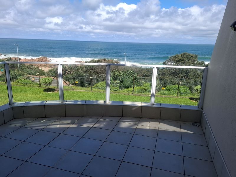 A spacious balcony featuring tiled flooring and a glass balustrade, offering expansive ocean and coastal views.