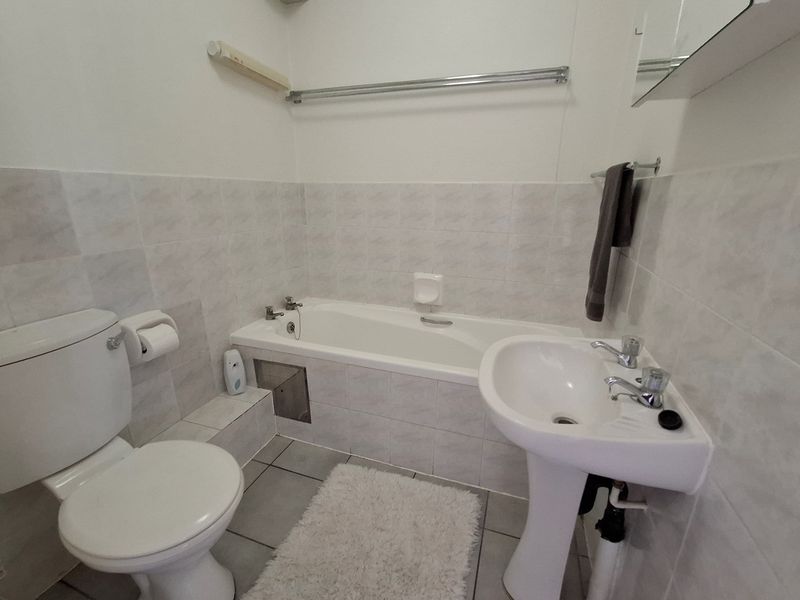 A functional bathroom featuring a standard bathtub, pedestal sink, and toilet with neutral wall and floor tiling.