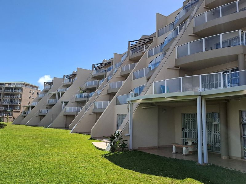 A view of the rear elevation of a multi-story apartment complex featuring tiered balconies, glass balustrades, and a well-maintained communal lawn area.