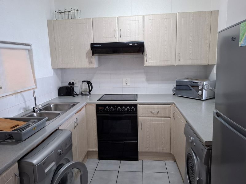 Compact kitchen featuring light wood-finish cabinetry, laminate countertops, tiled backsplash, and integrated electric cooking appliances.