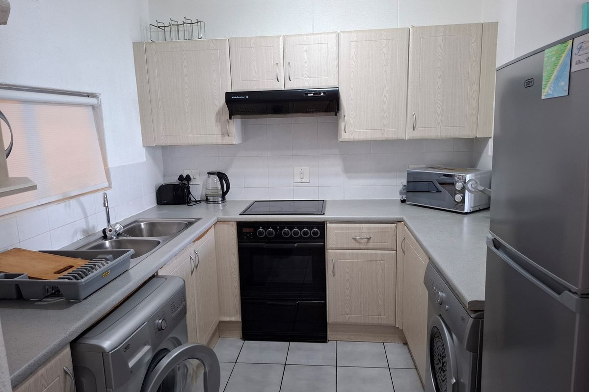 Compact kitchen featuring light wood-finish cabinetry, laminate countertops, tiled backsplash, and integrated electric cooking appliances.