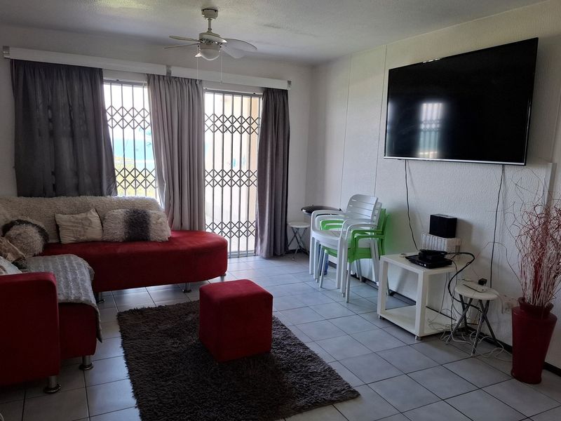 A living room featuring tiled flooring, a ceiling fan, and a security gate leading to an outdoor area.