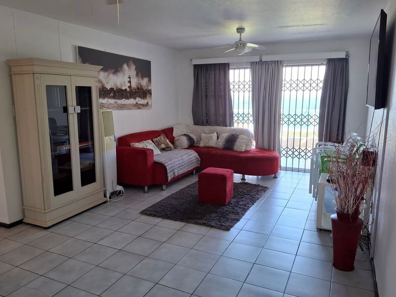 A living room featuring tiled flooring, a ceiling fan, and a sliding glass door with a security gate leading to an outdoor area.