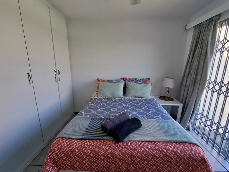 A functional bedroom featuring built-in cupboards, tiled flooring, and a security gate leading to an outdoor area.