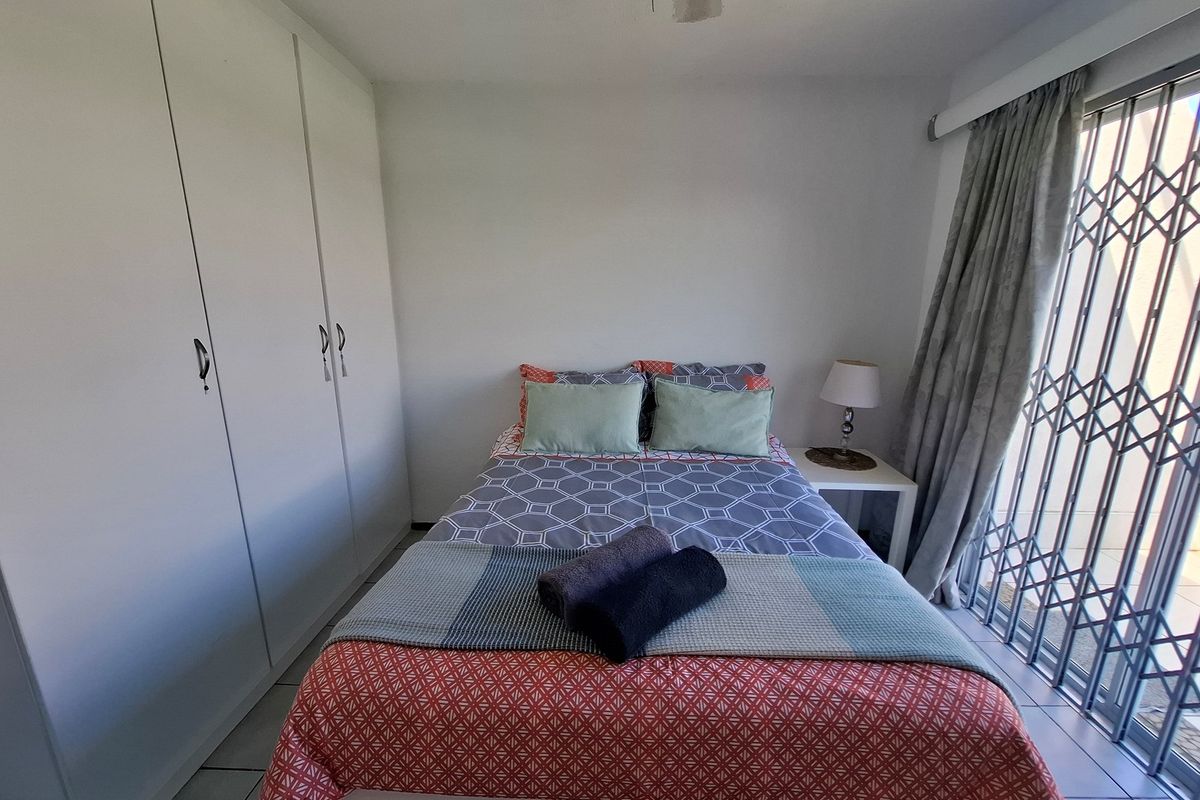 A functional bedroom featuring built-in cupboards, tiled flooring, and a security gate leading to an outdoor area.