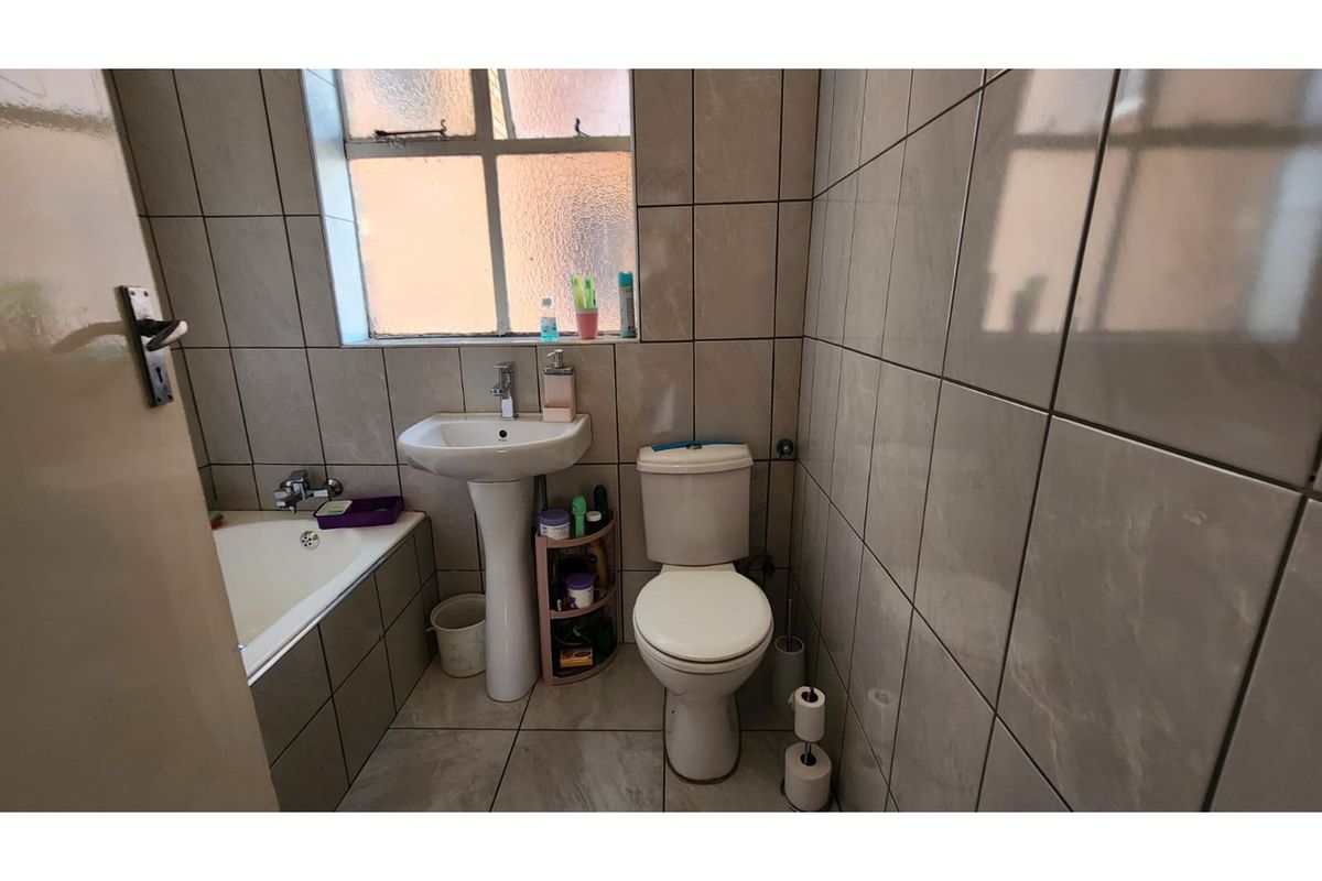 A compact bathroom featuring a pedestal basin, a standard toilet, and a built-in bathtub with full-height wall tiling.