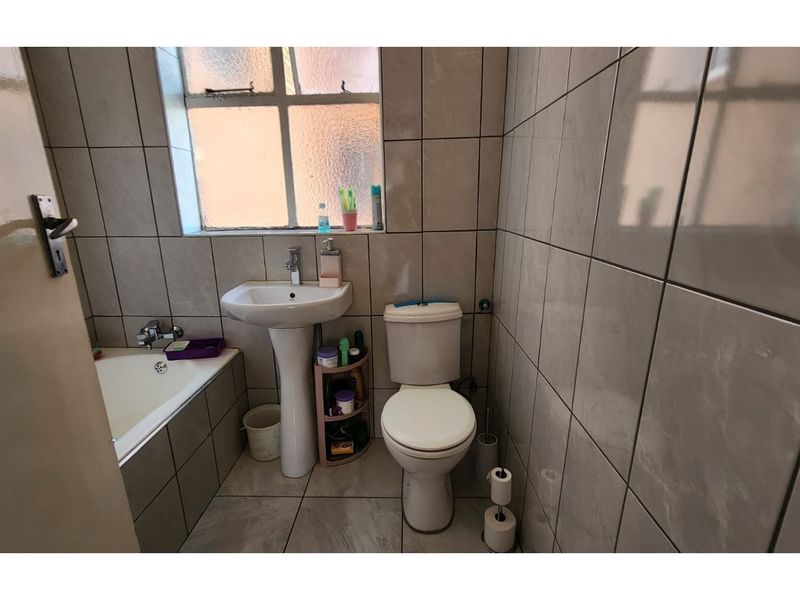 A compact bathroom featuring a pedestal basin, a standard toilet, and a built-in bathtub with full-height wall tiling.