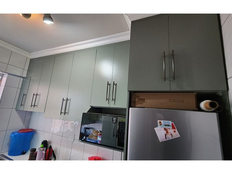 A modern kitchen featuring sage green cabinetry, tiled splashbacks, and a built-in microwave unit, offering a clean and functional cooking space.