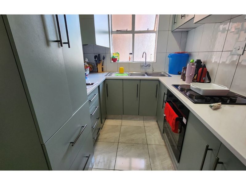 A compact, functional kitchen featuring modern grey cabinetry, white countertops, a built-in oven, hob, and a double-basin sink with tiled splashbacks.