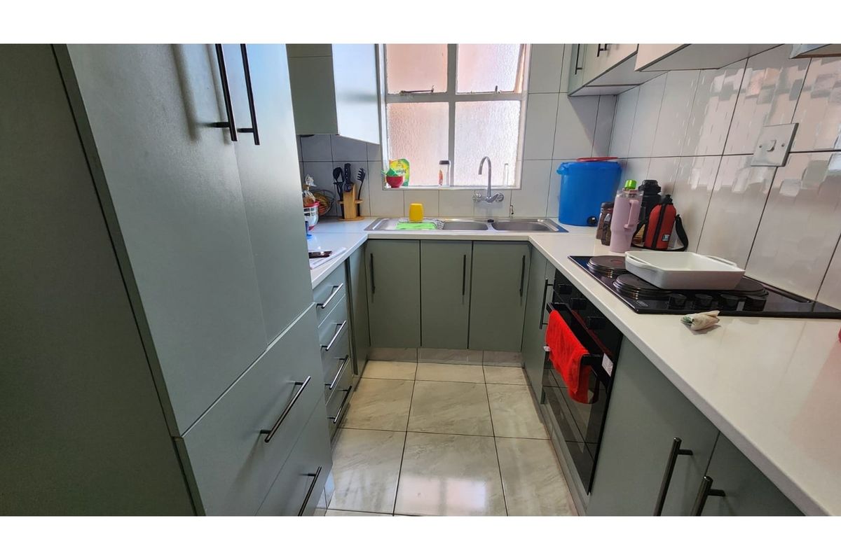 A compact, functional kitchen featuring modern grey cabinetry, white countertops, a built-in oven, hob, and a double-basin sink with tiled splashbacks.