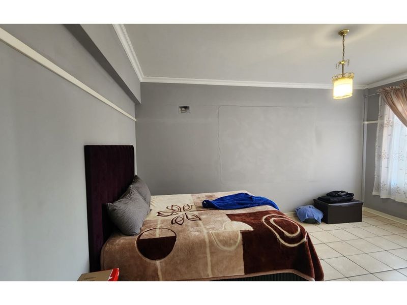 A spacious bedroom featuring tiled flooring, crown molding, and a central pendant light fixture.