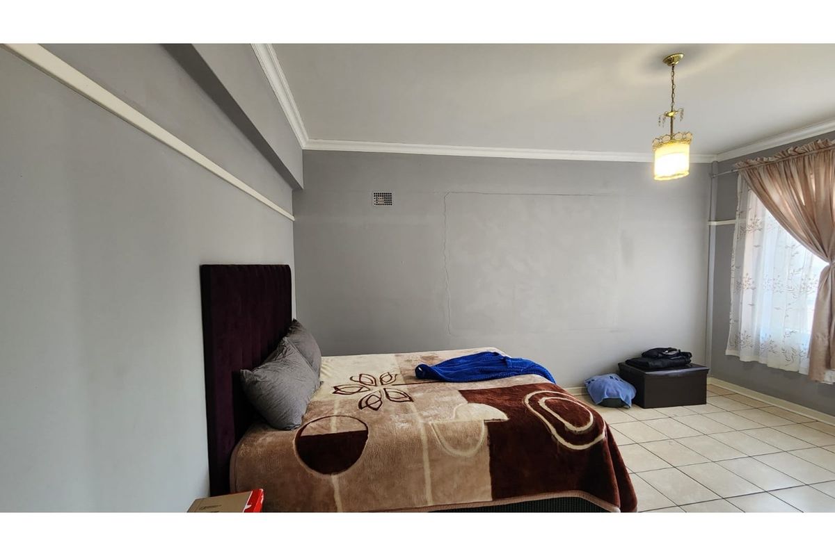 A spacious bedroom featuring tiled flooring, crown molding, and a central pendant light fixture.
