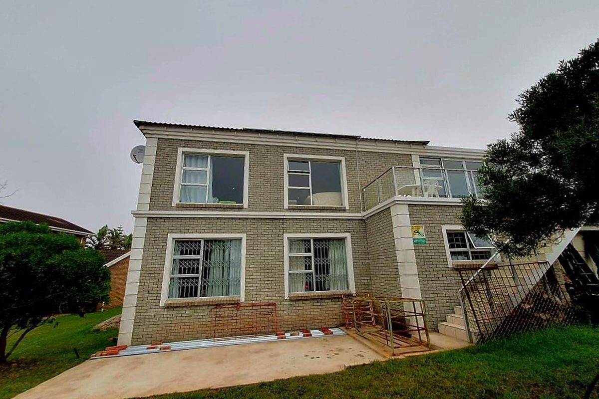 Rear view of a two-story brick house featuring a balcony with glass balustrades, security bars on windows, and a paved patio area.