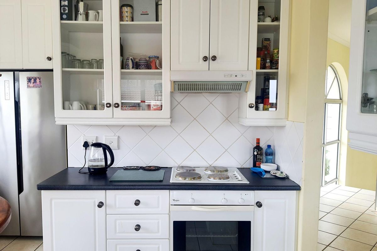 A functional kitchen featuring white cabinetry, a dark laminate countertop, a built-in oven, and a white hob with a matching extractor fan.