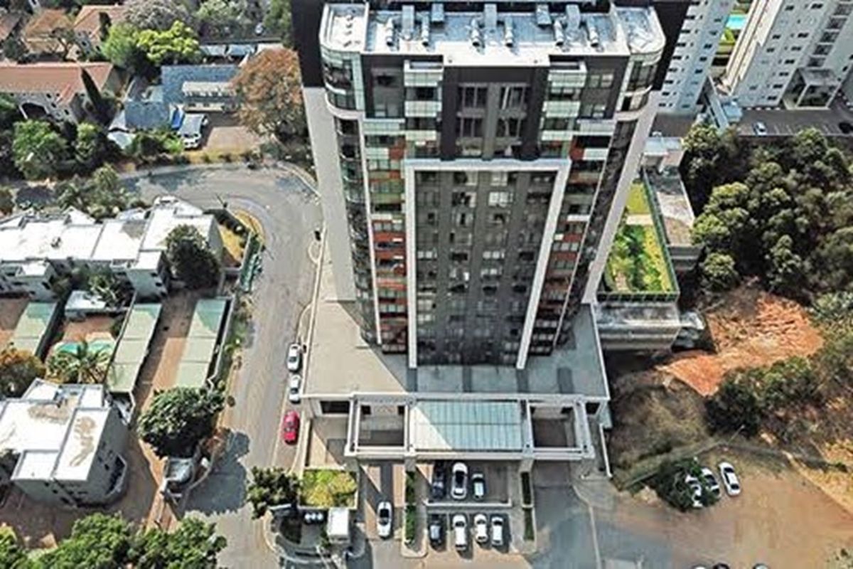 Aerial view of a modern high-rise apartment building featuring a prominent facade, glass balcony railings, and a ground-level entrance canopy.