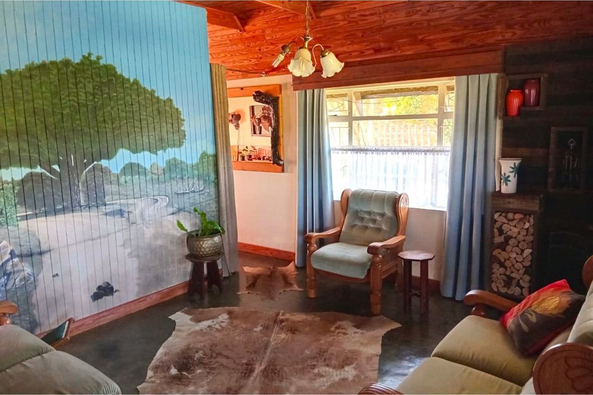 A rustic living room featuring a timber-clad ceiling, large window with natural light, and a unique hand-painted wall mural.