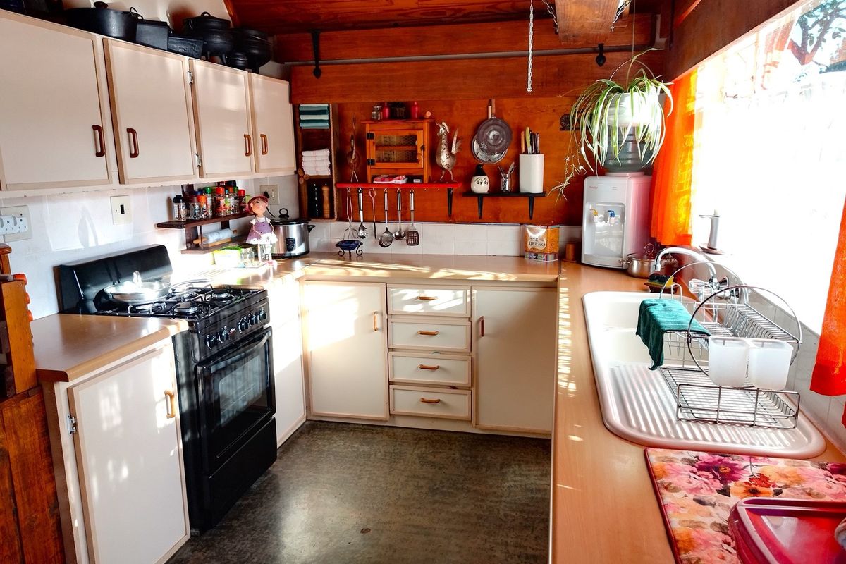 A functional kitchen featuring built-in cabinetry, a freestanding gas stove, and a double-basin sink with laminate countertops and timber wall paneling.