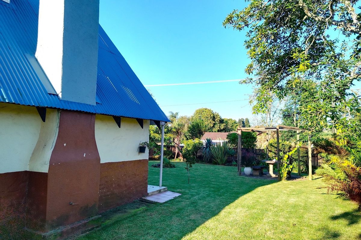 A view of the rear garden featuring a lawn, mature trees, a wooden pergola structure, and the side elevation of the house with a chimney.