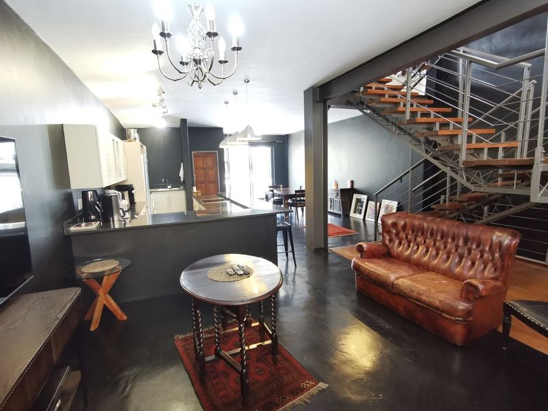 Spacious open-plan living area featuring a modern kitchen with island, industrial-style staircase, and dark finishes throughout.
