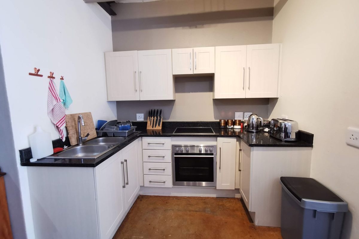 Compact kitchen featuring white cabinetry, granite countertops, and integrated stainless steel oven and hob, with a concrete floor finish.
