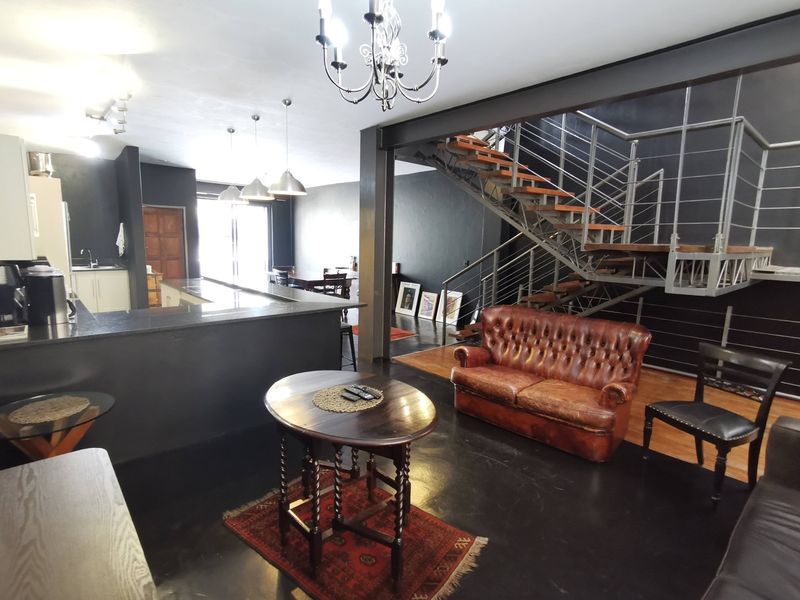 Spacious open-plan living area featuring a modern kitchen with island, dark flooring, and a striking architectural staircase with metal balustrades.