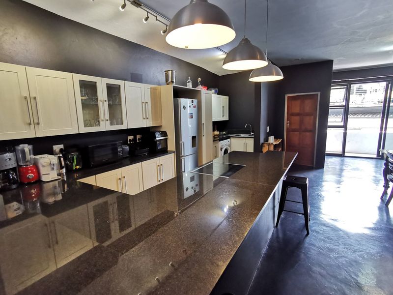 Modern open-plan kitchen featuring dark cabinetry, granite countertops, and polished concrete floors, seamlessly flowing into the living and dining area.