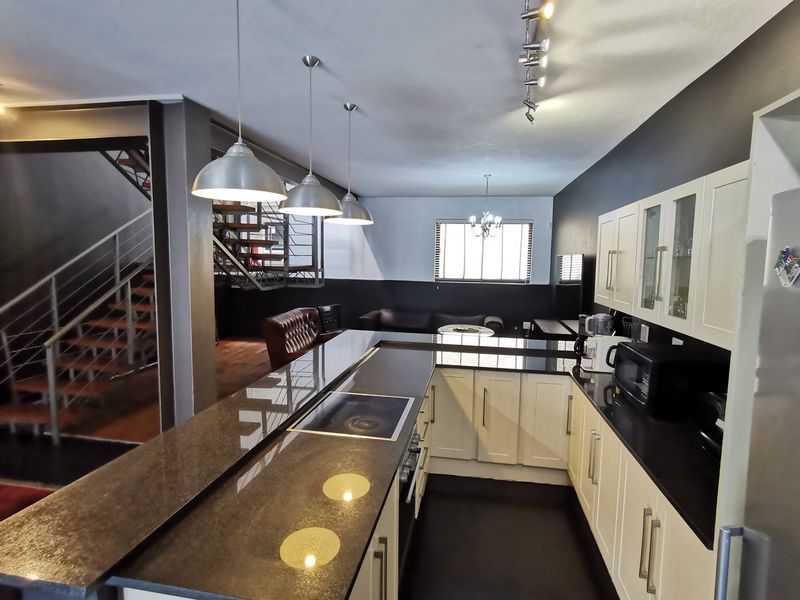 Open-plan kitchen featuring granite countertops, built-in cabinetry, and a modern staircase, seamlessly flowing into the living area with contemporary lighting fixtures.