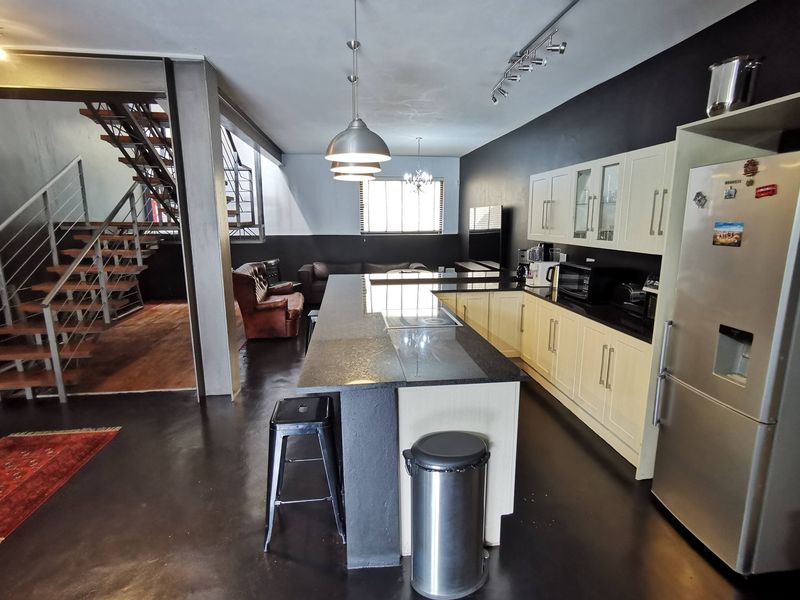 Spacious open-plan living area featuring a modern kitchen with granite island, sleek cabinetry, and an industrial-style staircase with steel accents.