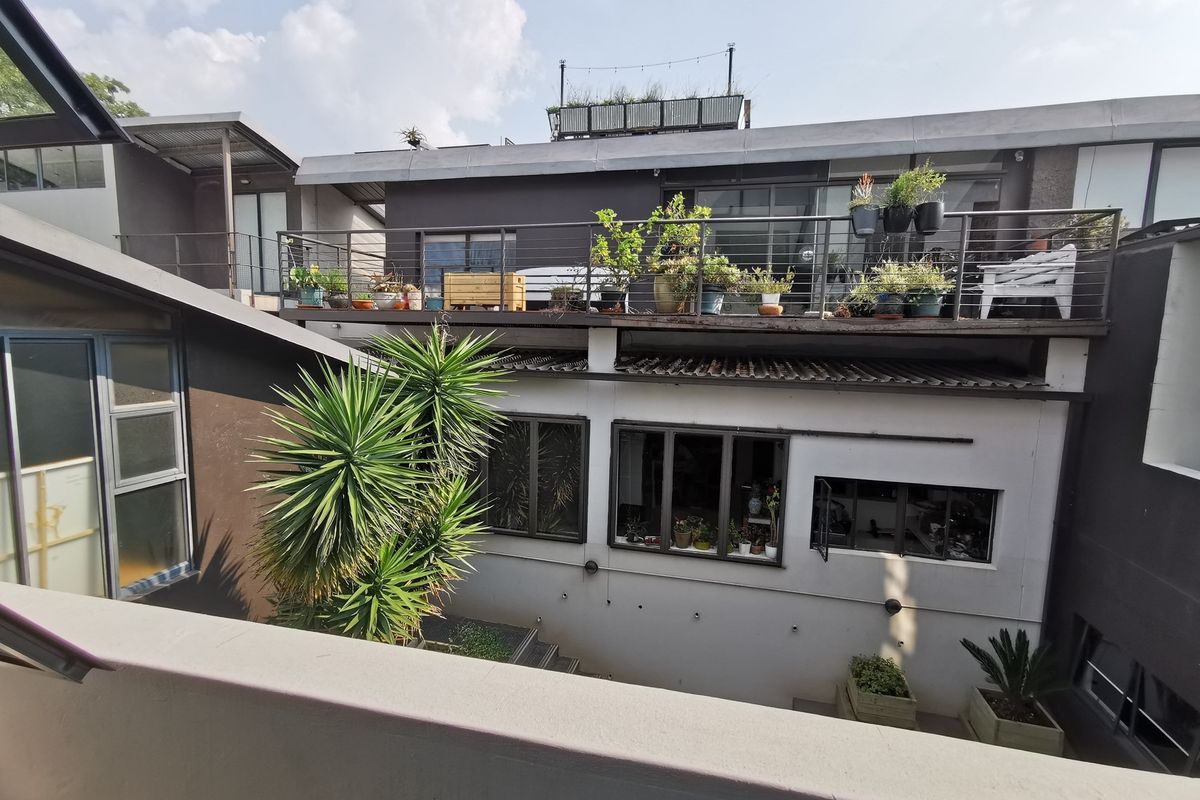 Rear view of the apartment building featuring a private balcony with metal railings and large sliding glass doors overlooking a lower courtyard area.