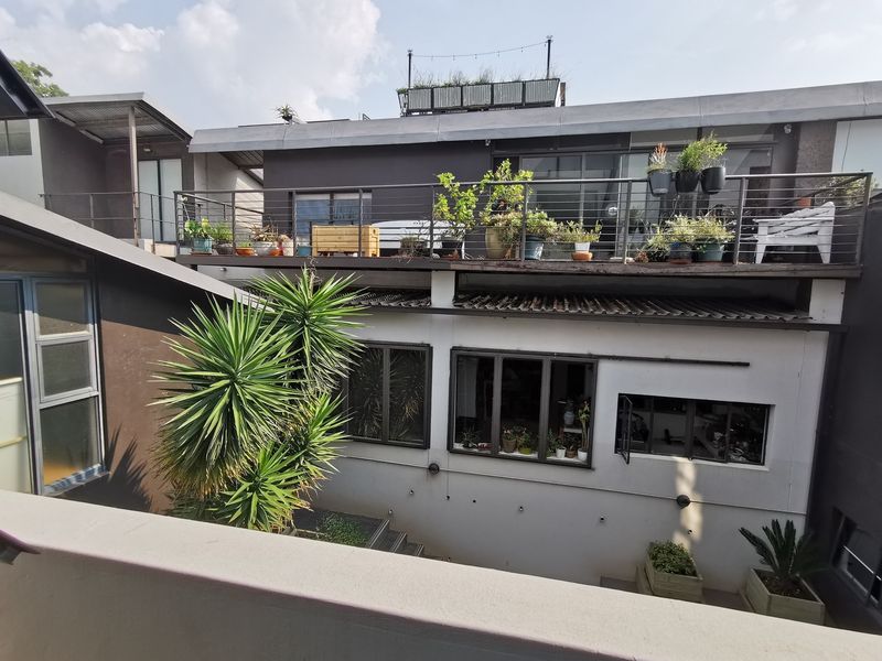 Rear view of the apartment building featuring a private balcony with metal railings and large sliding glass doors overlooking a lower courtyard area.