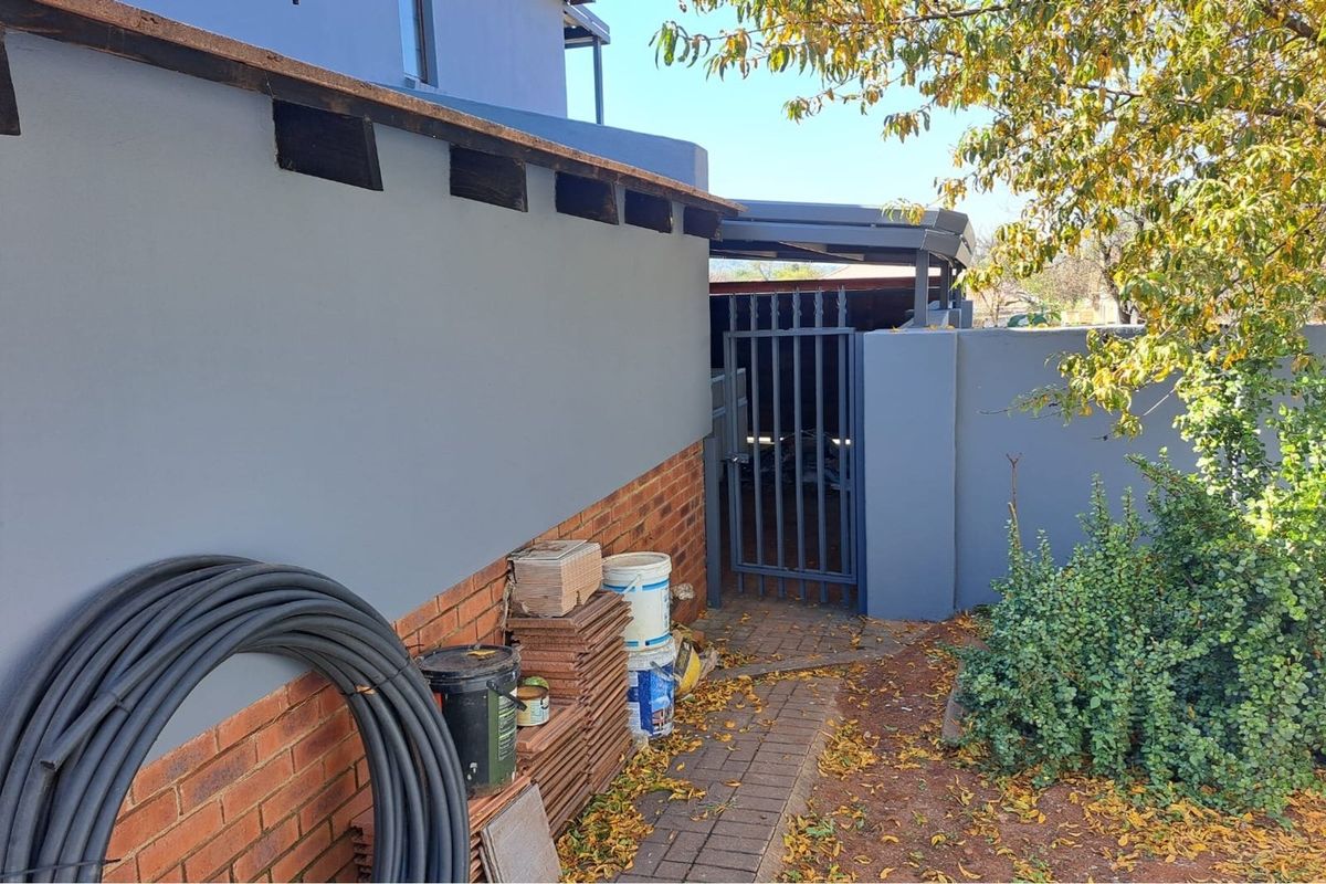 A side exterior view of the property featuring a paved walkway, a secure metal gate, and a painted boundary wall with exposed brick accents.