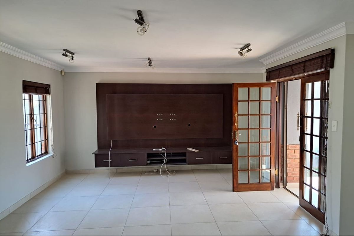 Spacious living room featuring a built-in dark wood media console, tiled flooring, and glass-paned French doors leading to an outdoor area.