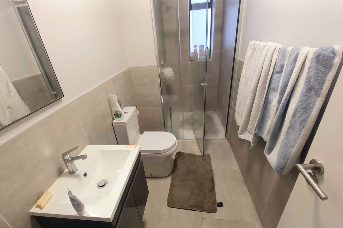 A modern bathroom featuring a vanity basin, toilet, and a glass-enclosed shower with neutral wall and floor tiling.
